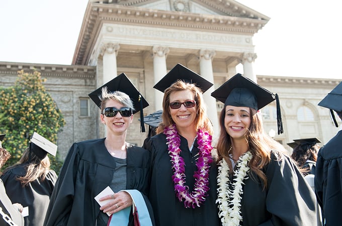 Three female students from the School of Education gather in front of the Administration Building after commencement.