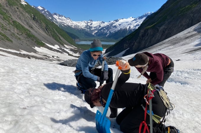 Three people perform scientific research on a glacier in Alaska.
