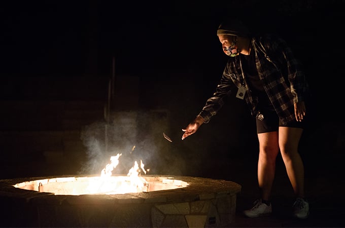 A student throws a piece of paper into a bonfire at night.