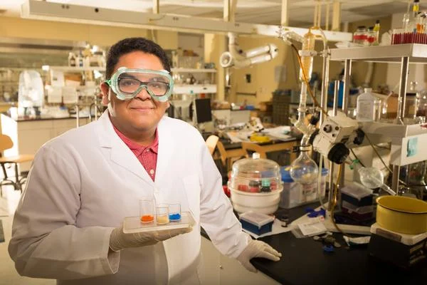 A man in a lab coat holds samples in front of a laboratory