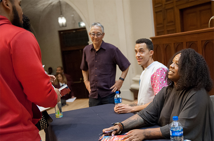 Speakers sit at a table to sign books while greeting members of the audience.