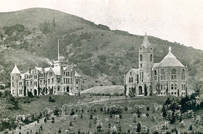 Two buildings sit on a hill in a historic black and white photograph.